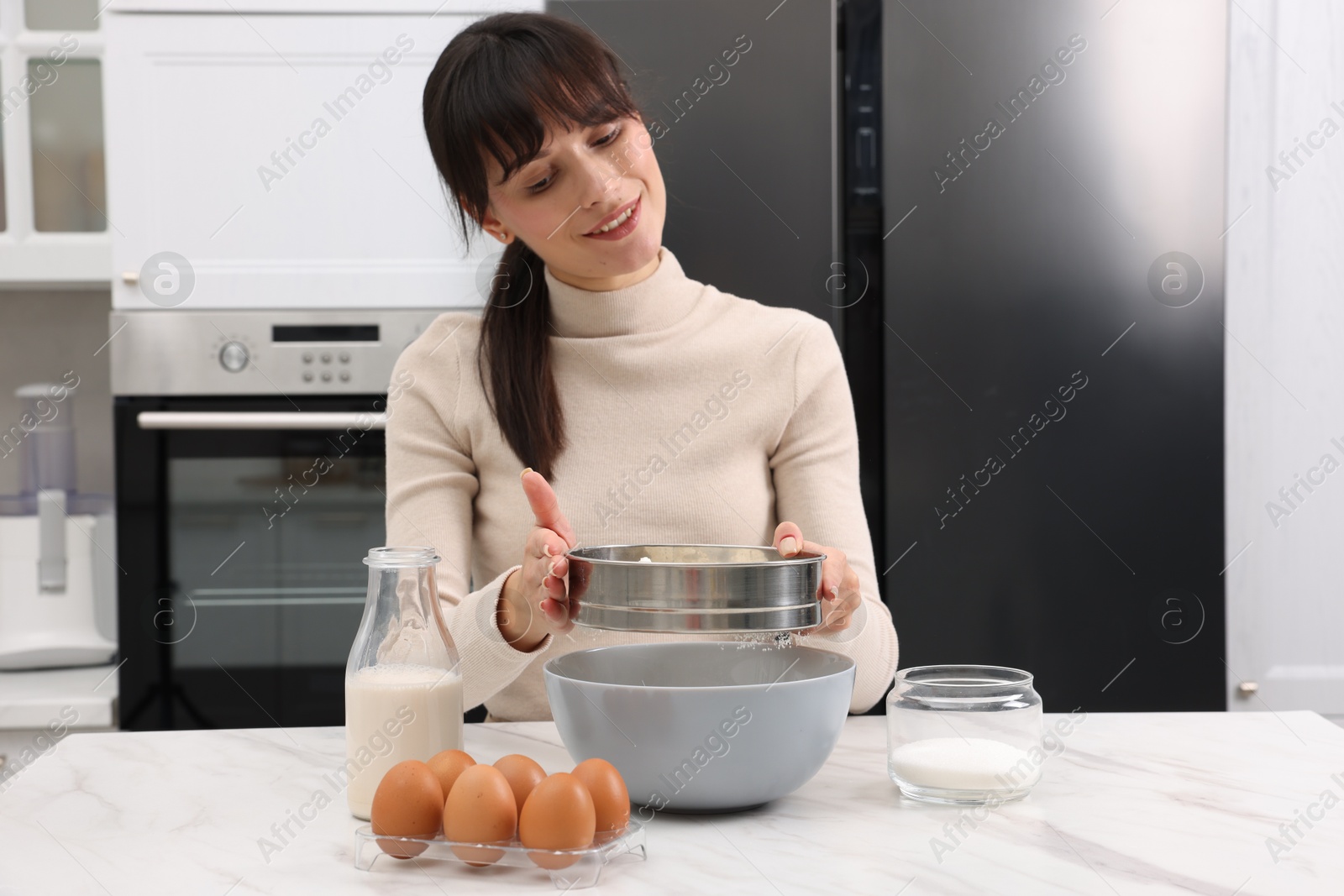 Photo of Making dough. Woman sifting flour into bowl at white table. Space for text