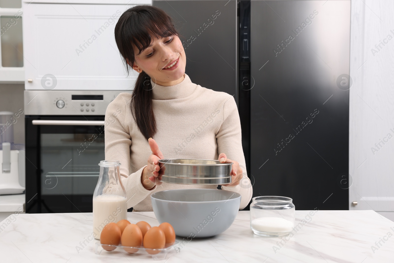 Photo of Making dough. Woman sifting flour into bowl at white table. Space for text