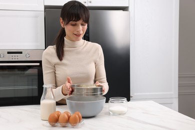 Photo of Making dough. Woman sifting flour into bowl at white table. Space for text