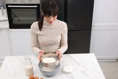 Photo of Making dough. Woman sifting flour into bowl at white table. Space for text