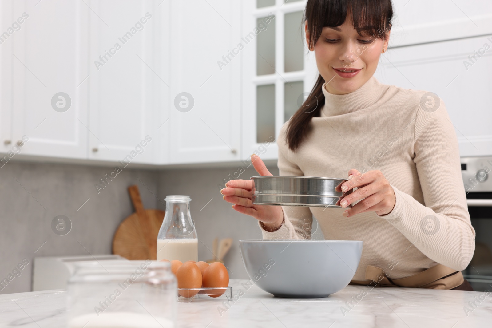 Photo of Making dough. Woman sifting flour into bowl at white table. Space for text