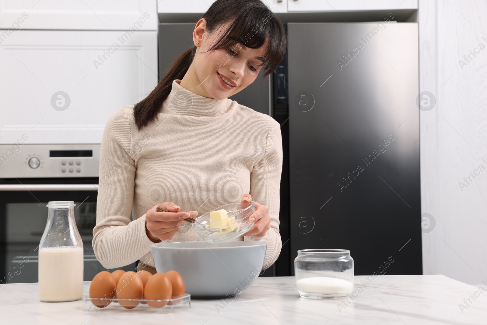 Photo of Making dough. Woman adding butter into bowl at white marble table