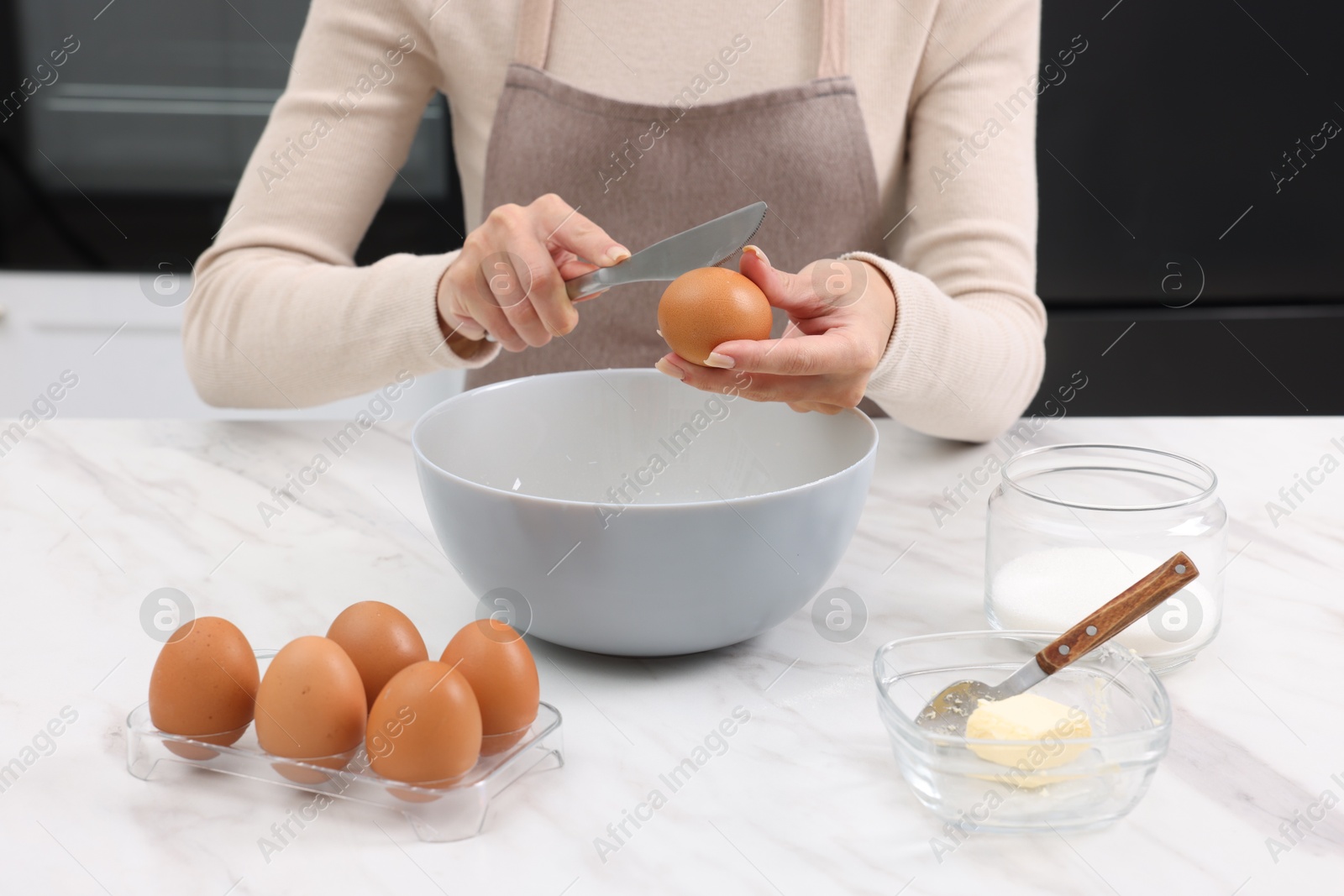 Photo of Making dough. Woman adding egg into bowl at white marble table, closeup