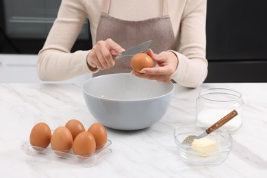 Photo of Making dough. Woman adding egg into bowl at white marble table, closeup