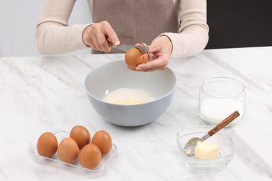 Photo of Making dough. Woman adding egg into bowl at white marble table, closeup