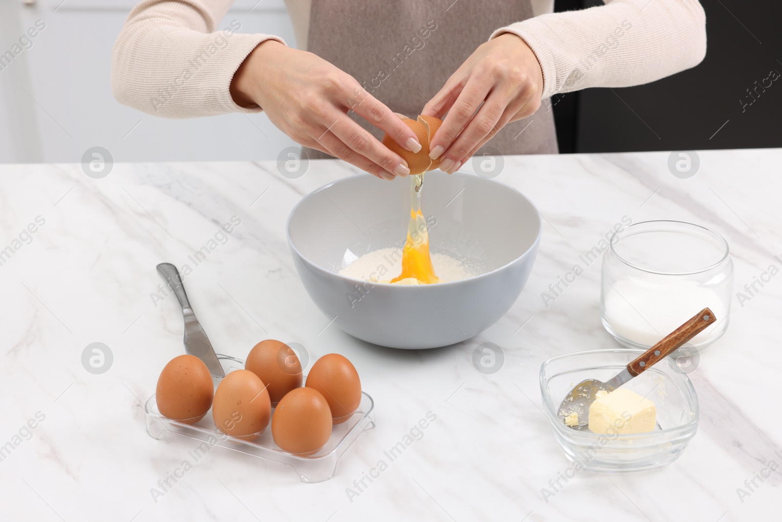 Photo of Making dough. Woman adding egg into bowl at white marble table, closeup