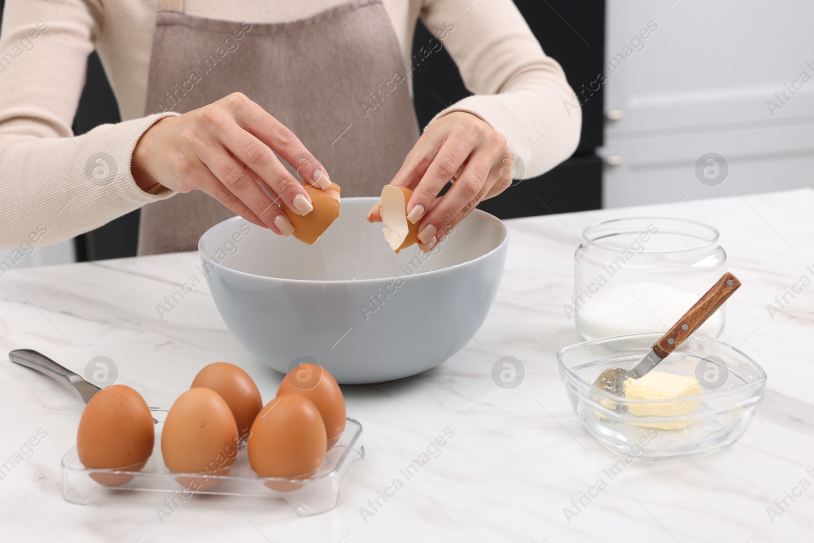 Photo of Making dough. Woman adding egg into bowl at white marble table, closeup