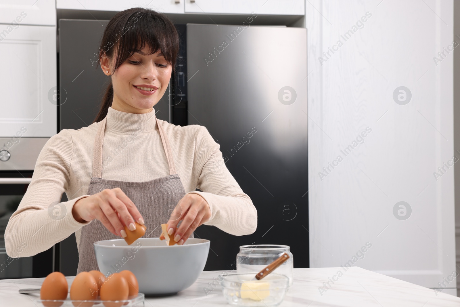 Photo of Making dough. Woman adding egg into bowl at white marble table. Space for text