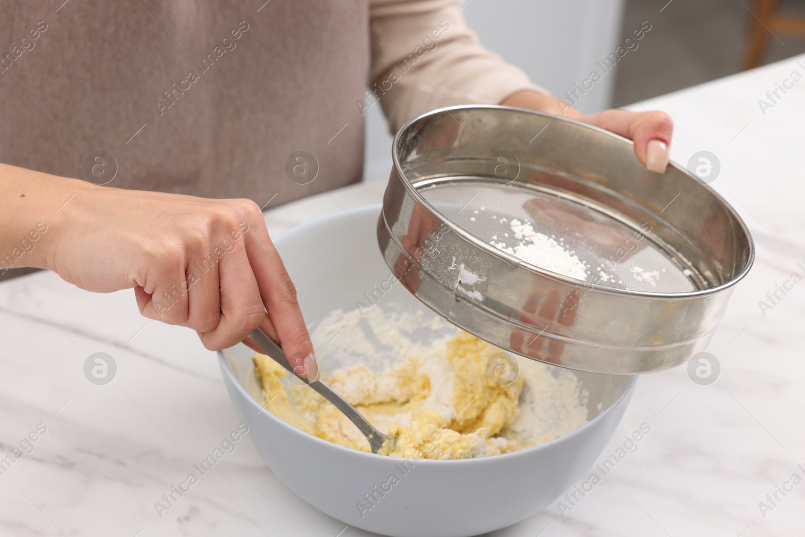 Photo of Woman sifting flour into bowl with dough at white marble table, closeup