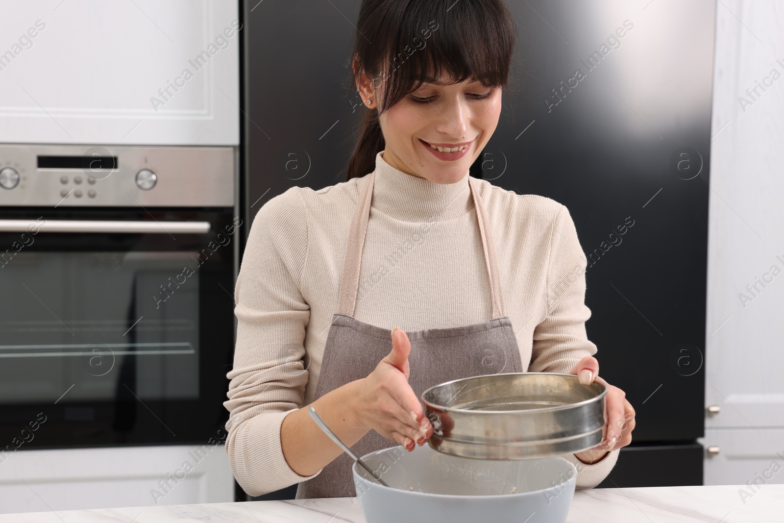 Photo of Woman sifting flour into bowl with dough at white marble table