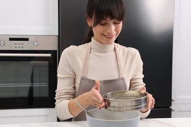 Woman sifting flour into bowl with dough at white marble table