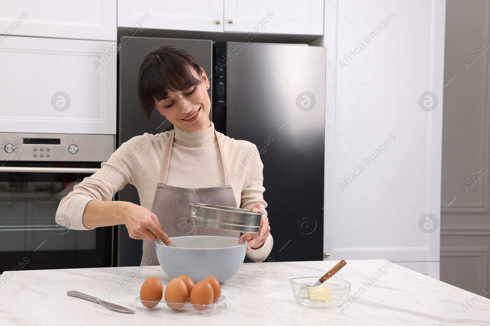 Photo of Woman sifting flour into bowl with dough at white marble table. Space for text