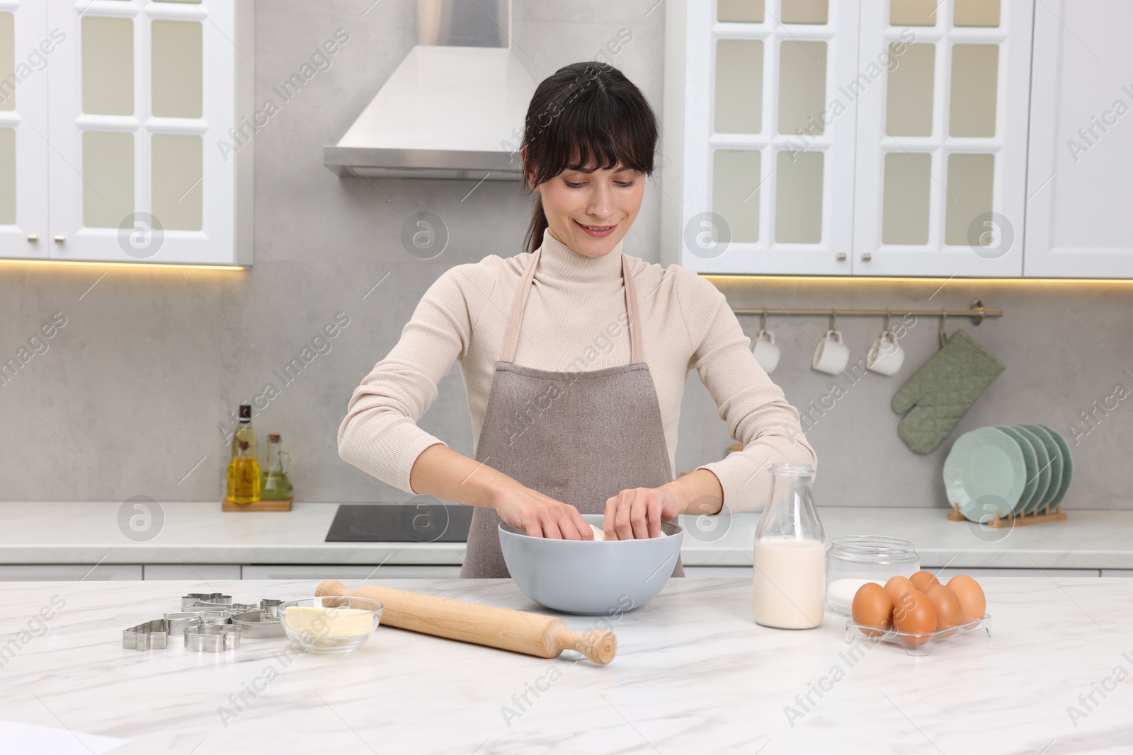 Photo of Woman kneading dough in bowl at white marble table