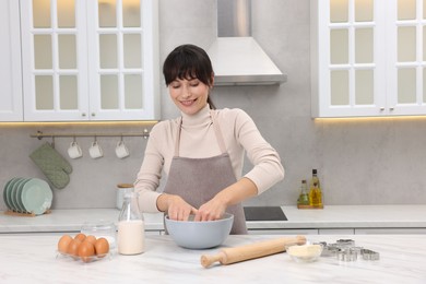 Woman kneading dough in bowl at white marble table