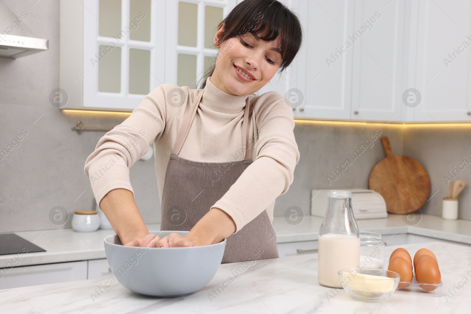 Photo of Woman kneading dough in bowl at white marble table