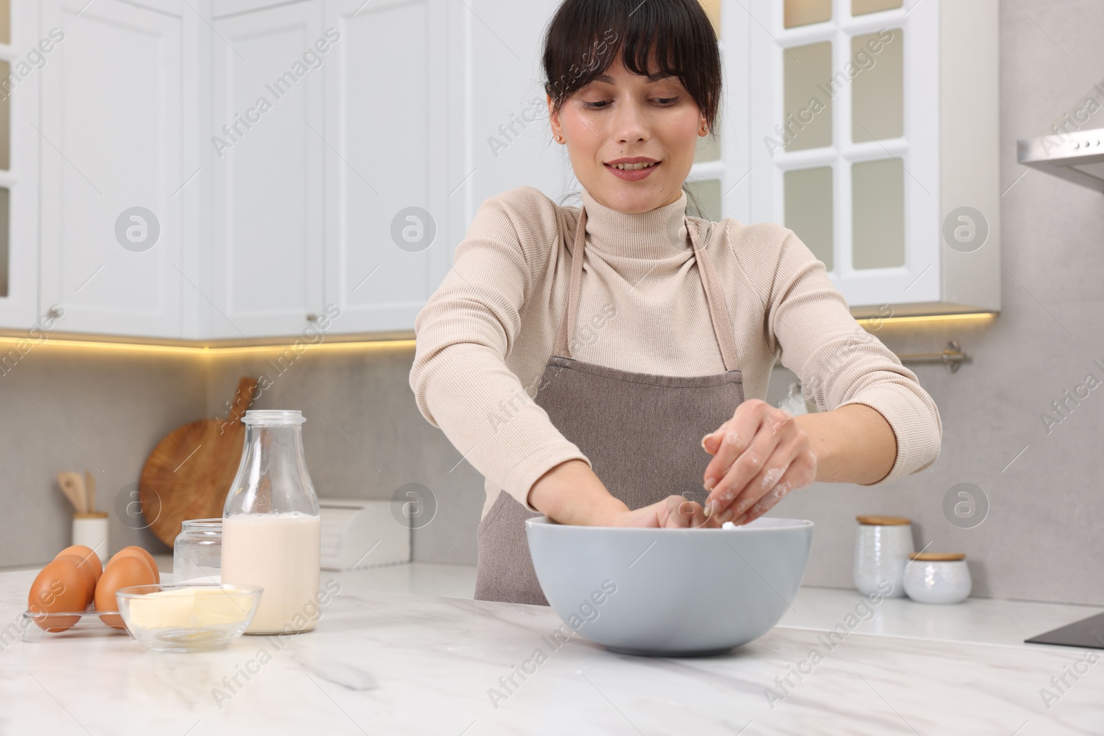 Photo of Woman kneading dough in bowl at white marble table