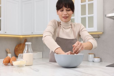 Woman kneading dough in bowl at white marble table