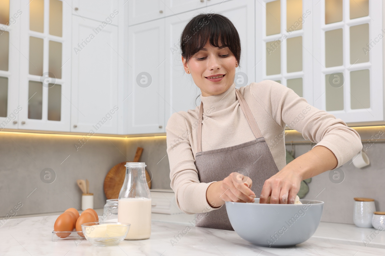 Photo of Woman kneading dough in bowl at white marble table