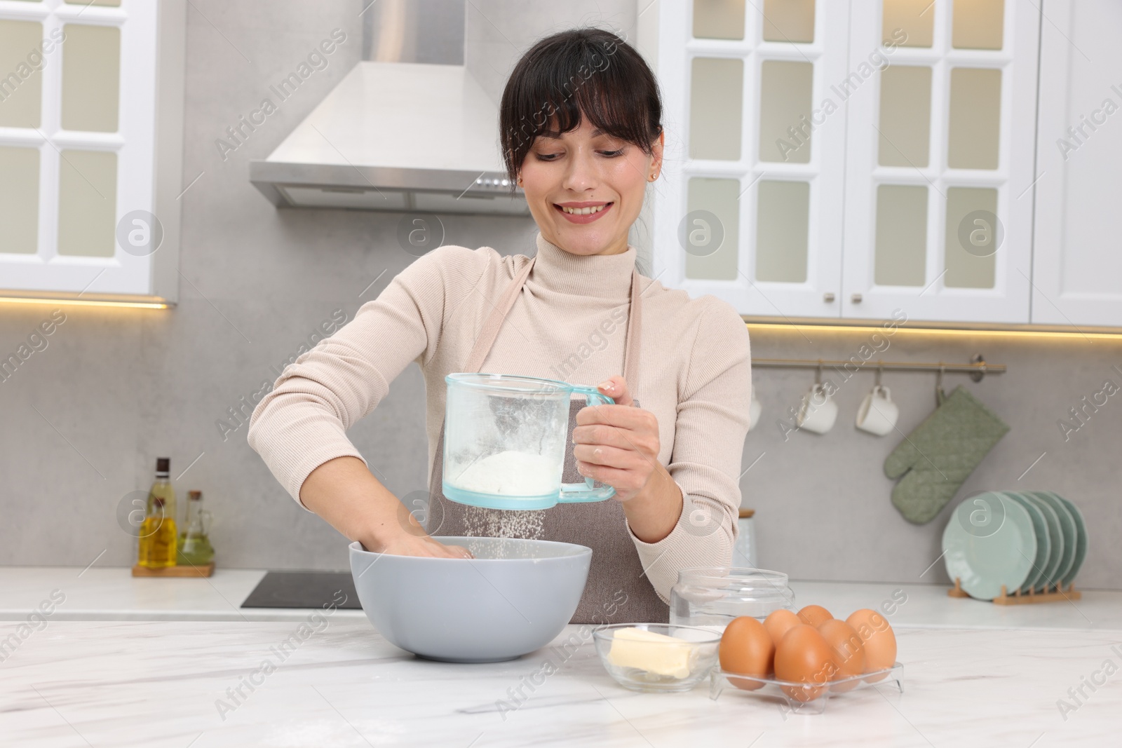 Photo of Woman sifting flour into bowl with dough at white marble table