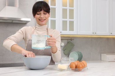 Photo of Woman sifting flour into bowl with dough at white marble table. Space for text