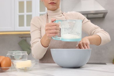 Photo of Woman sifting flour into bowl with dough at white marble table, closeup