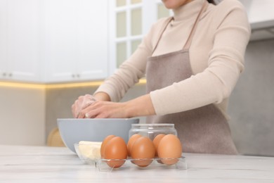 Woman kneading dough in bowl at white table, closeup