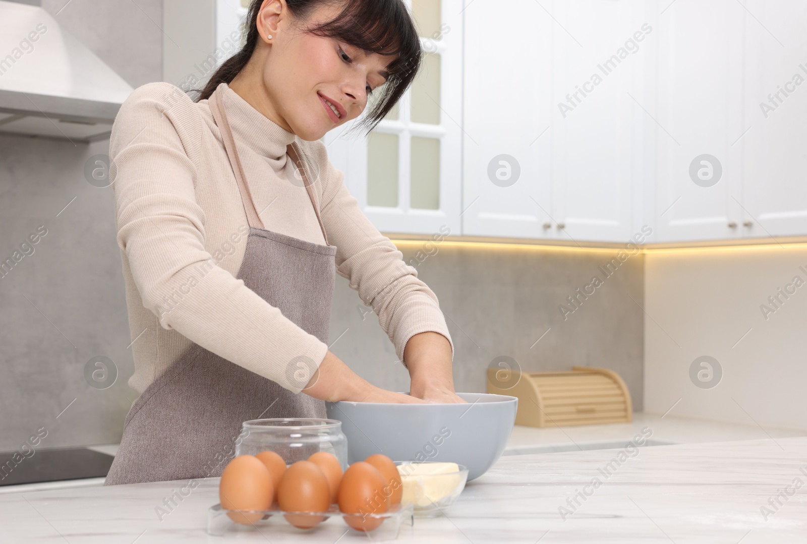 Photo of Woman kneading dough in bowl at white table. Space for text