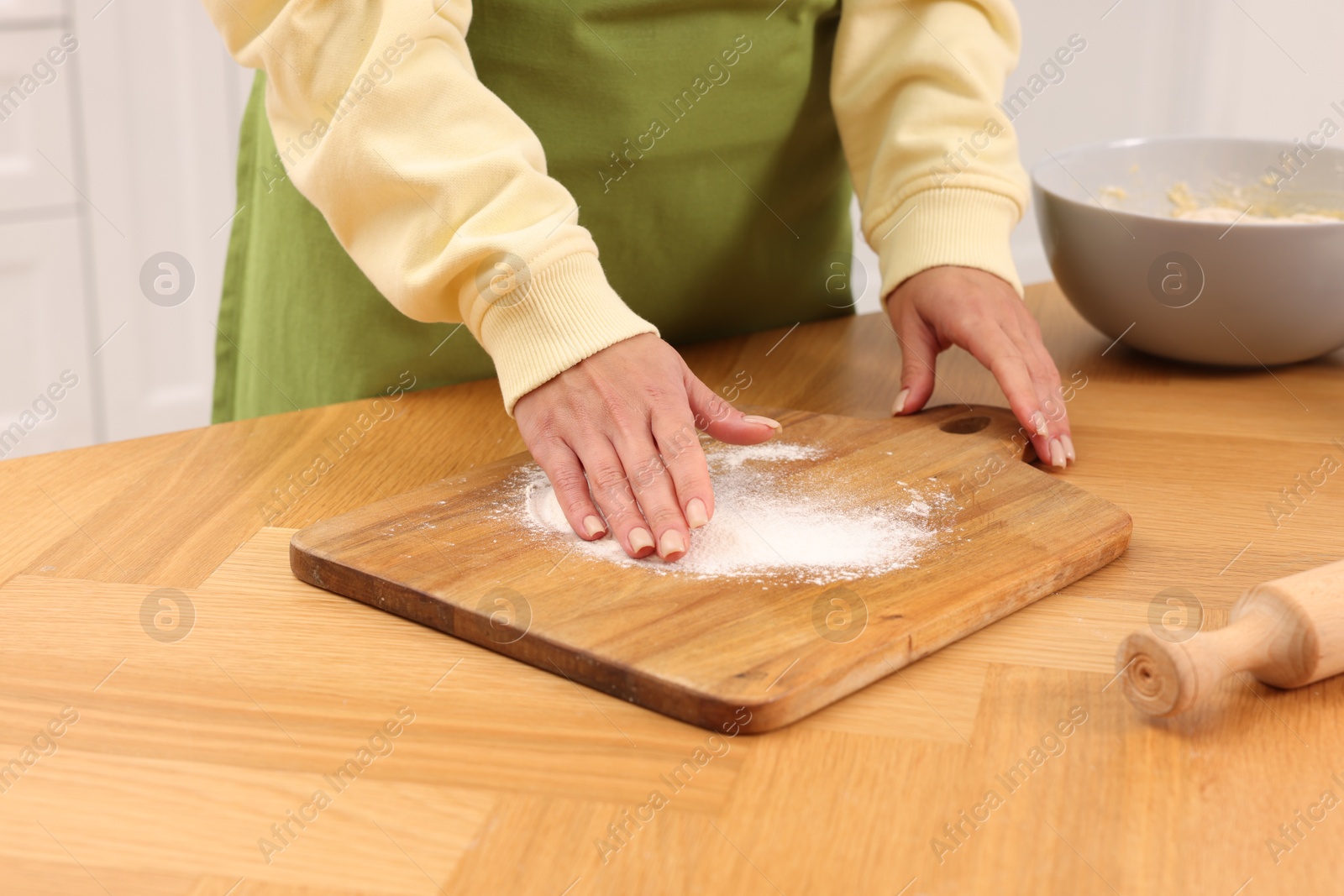 Photo of Woman sprinkling flour onto wooden board before rolling dough at table indoors, closeup