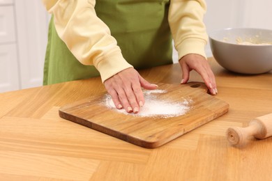 Photo of Woman sprinkling flour onto wooden board before rolling dough at table indoors, closeup