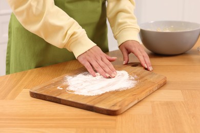 Photo of Woman sprinkling flour onto wooden board before rolling dough at table indoors, closeup