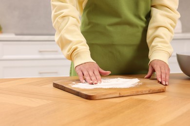 Photo of Woman sprinkling flour onto wooden board before rolling dough at table indoors, closeup