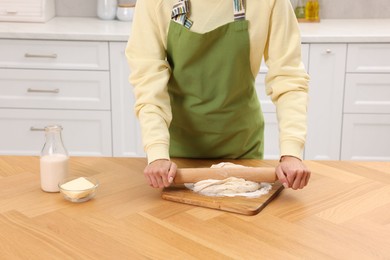 Photo of Woman rolling dough at wooden table indoors, closeup