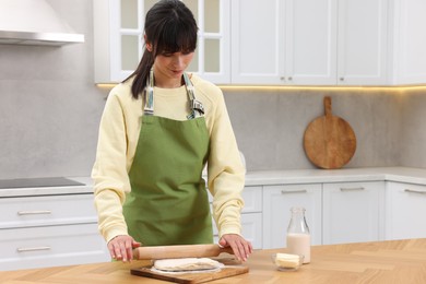 Photo of Woman rolling dough at wooden table indoors