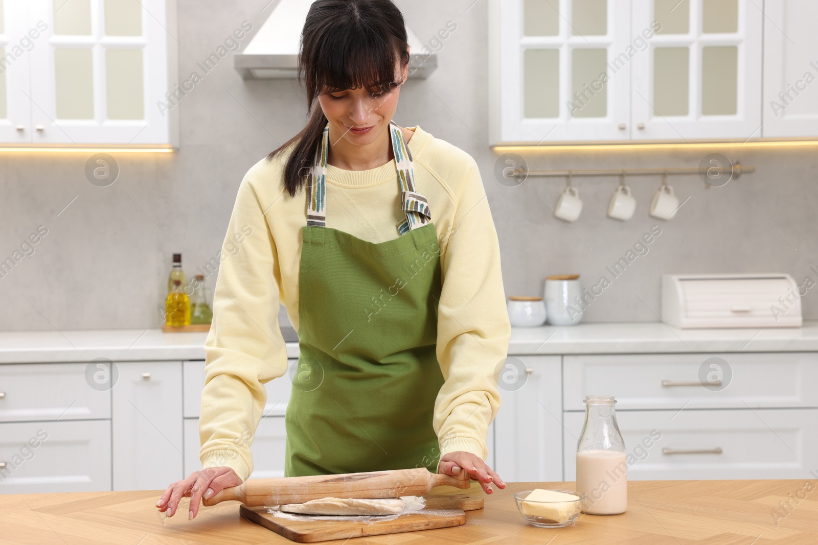 Photo of Woman rolling dough at wooden table indoors