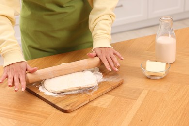 Woman rolling dough at wooden table indoors, closeup