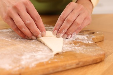 Woman making croissant at wooden table, closeup