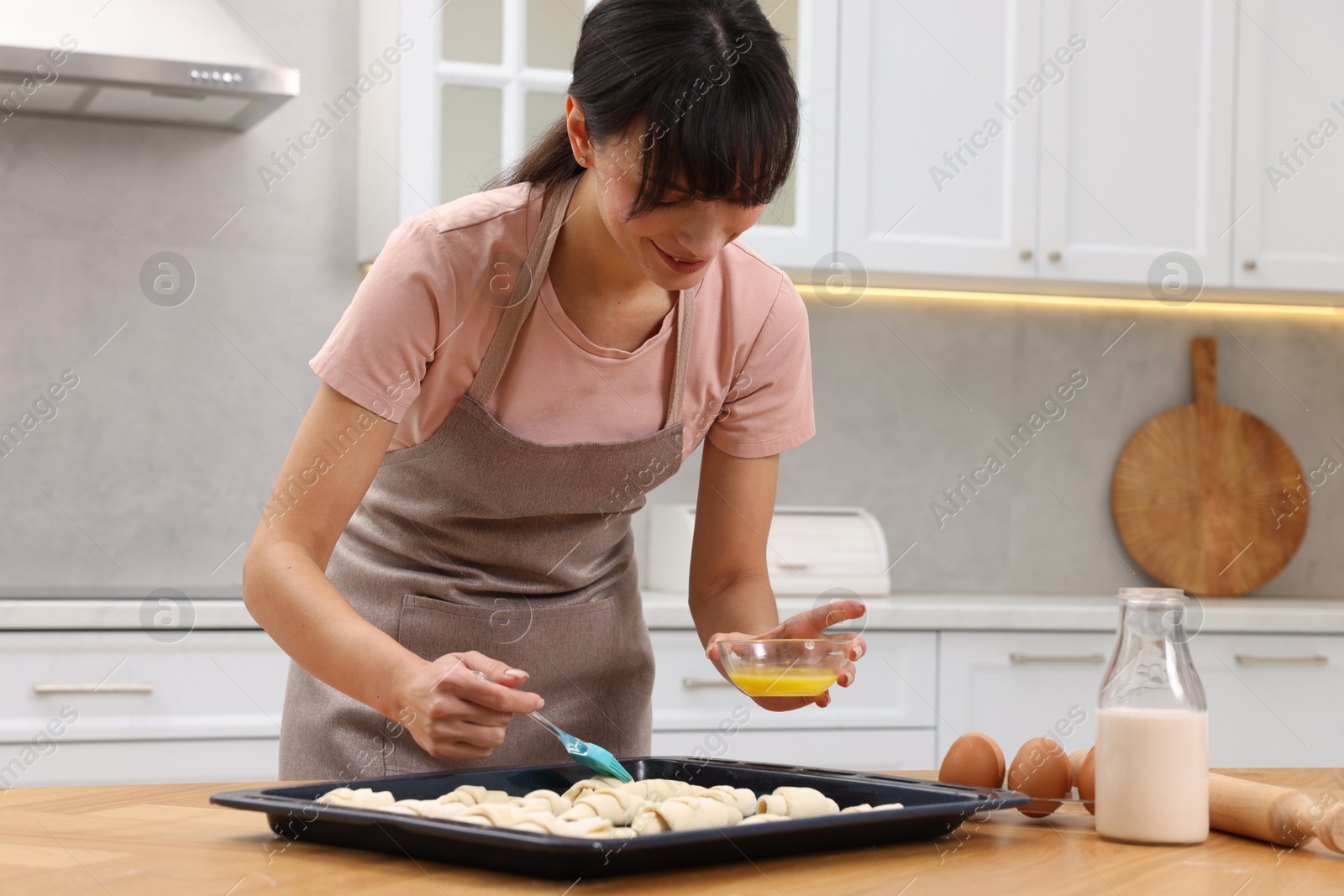 Photo of Woman brushing egg wash onto raw croissants at table indoors