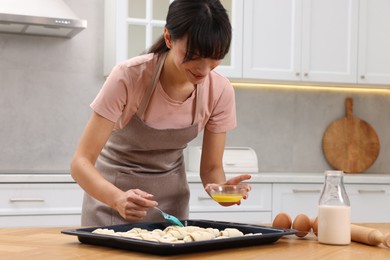 Woman brushing egg wash onto raw croissants at table indoors