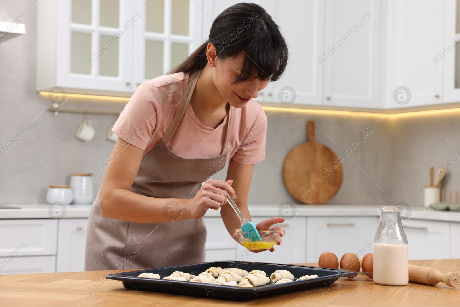 Photo of Woman brushing egg wash onto raw croissants at table indoors