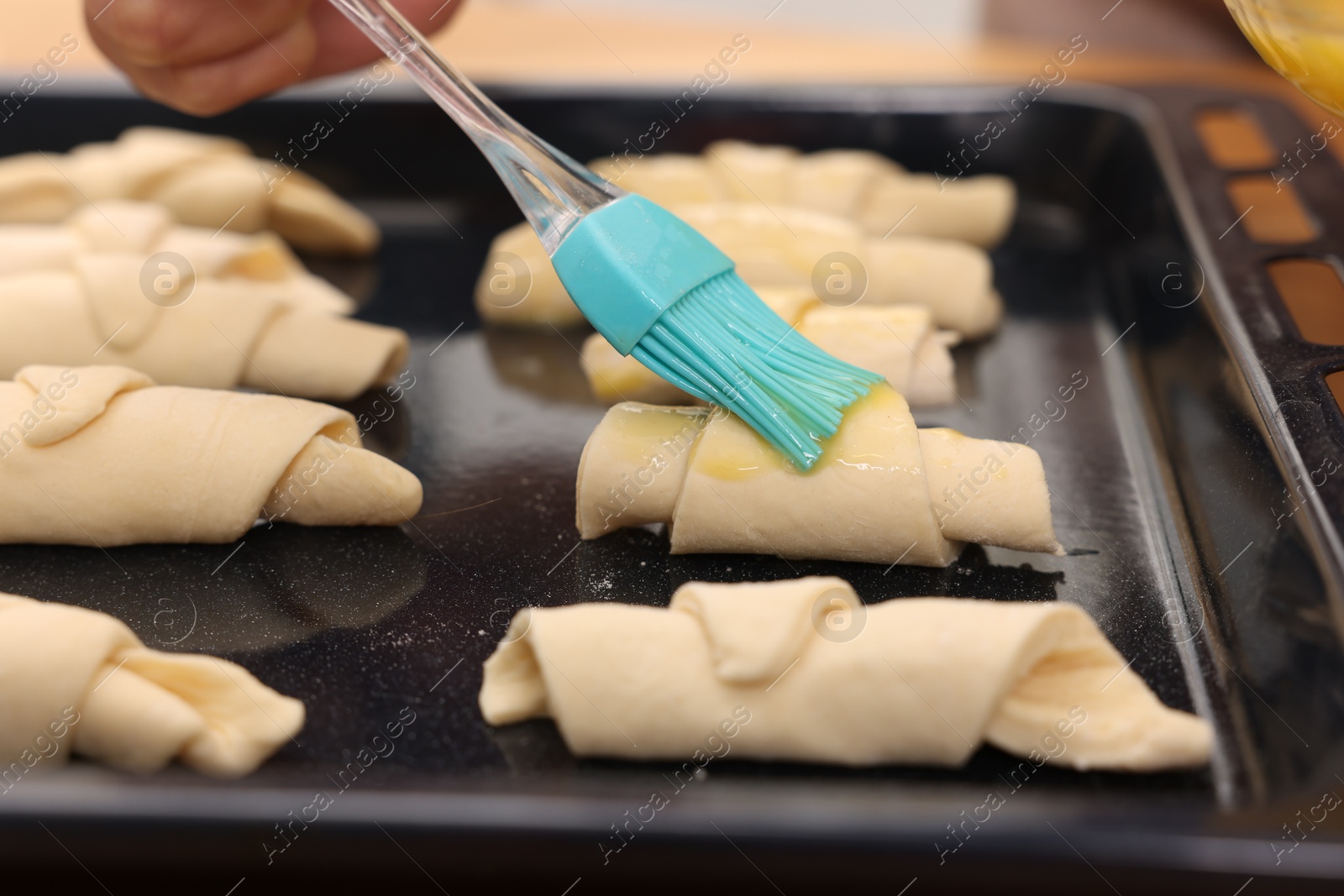 Photo of Woman brushing egg wash onto raw croissants at table indoors, closeup