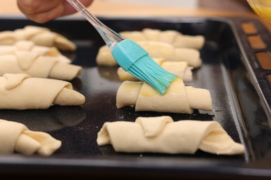 Woman brushing egg wash onto raw croissants at table indoors, closeup