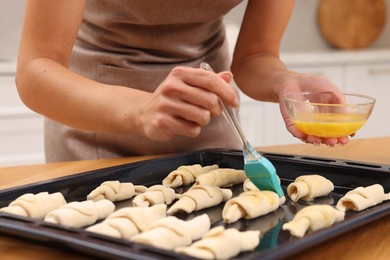 Woman brushing egg wash onto raw croissants at table indoors, closeup