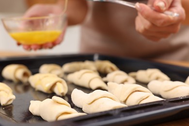 Woman brushing egg wash onto raw croissants at table indoors, closeup