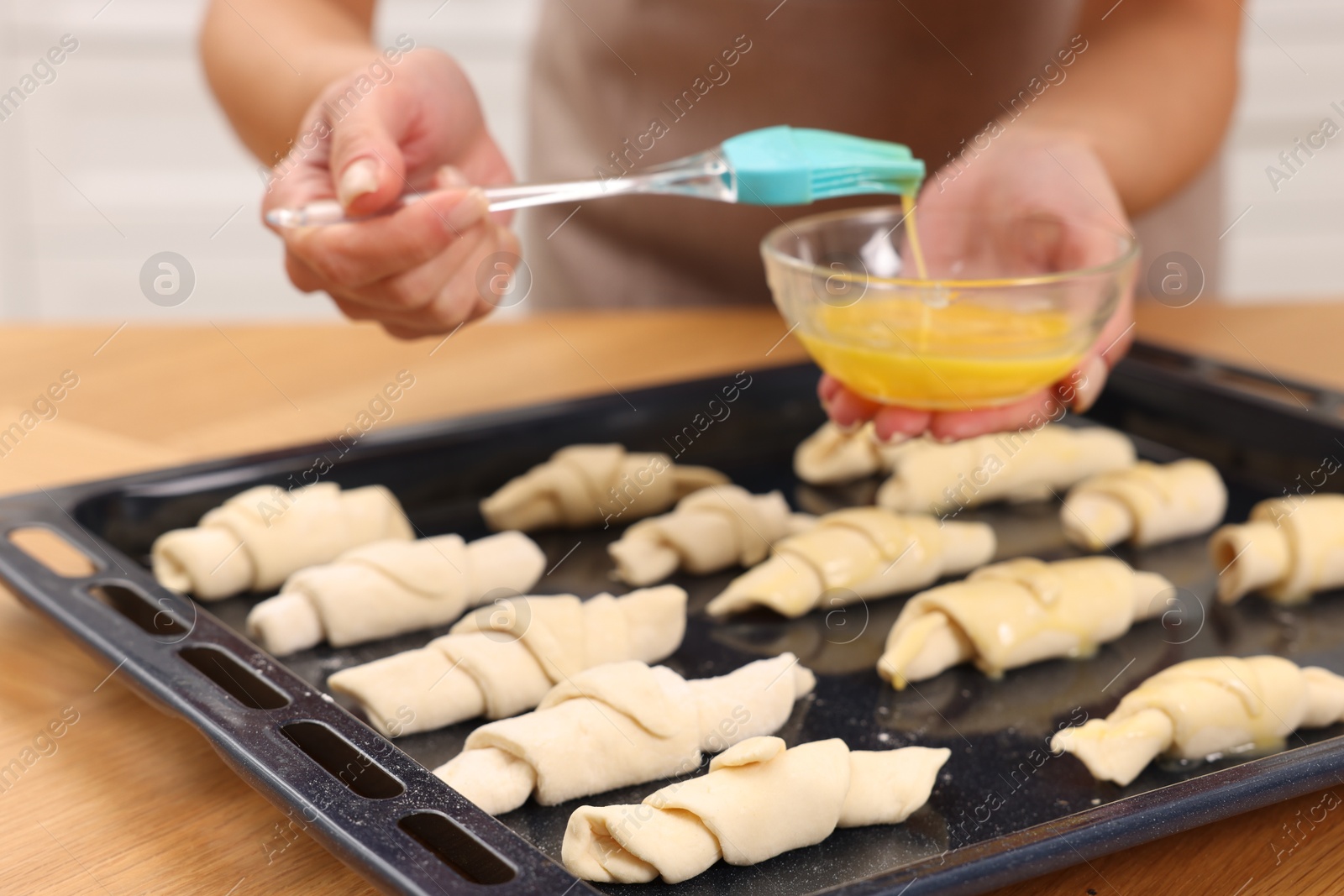 Photo of Woman brushing egg wash onto raw croissants at table indoors, closeup