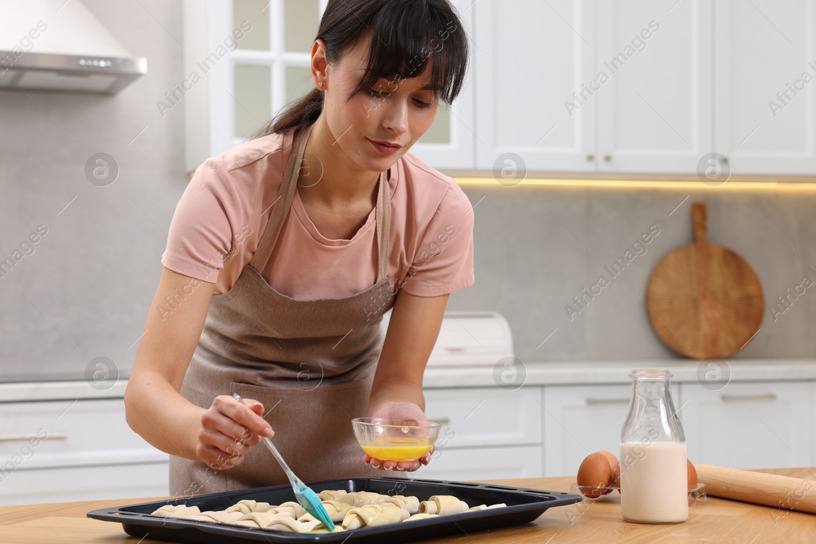 Photo of Woman brushing egg wash onto raw croissants at table indoors. Space for text