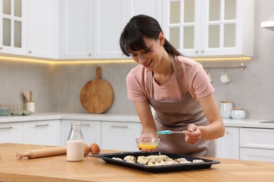 Photo of Woman brushing egg wash onto raw croissants at table indoors. Space for text