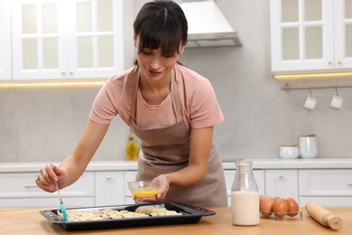 Woman brushing egg wash onto raw croissants at table indoors