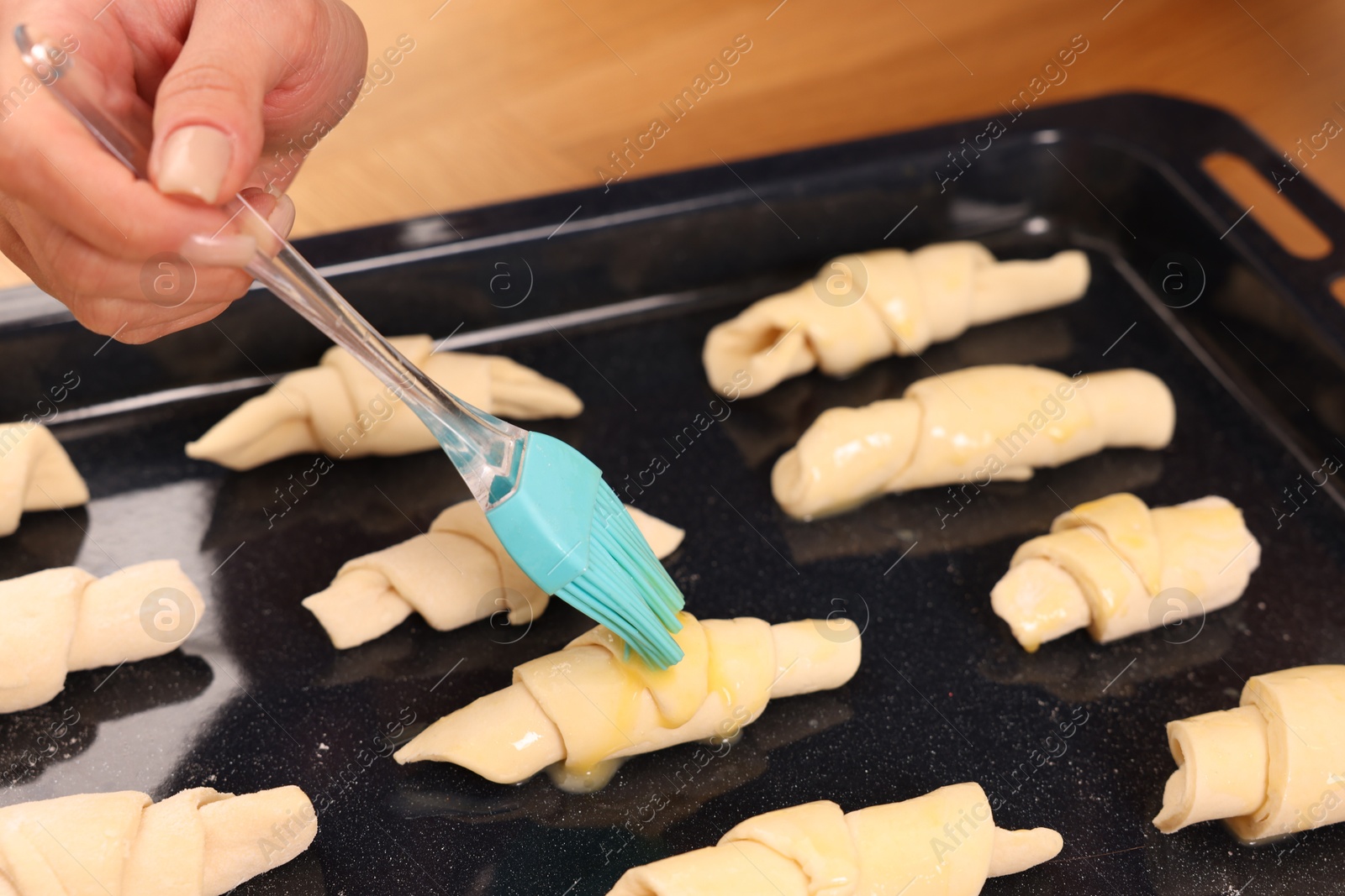 Photo of Woman brushing egg wash onto raw croissants at table indoors, closeup