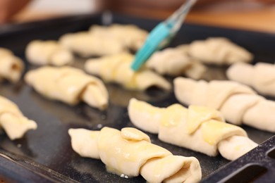 Photo of Woman brushing egg wash onto raw croissants at table indoors, closeup