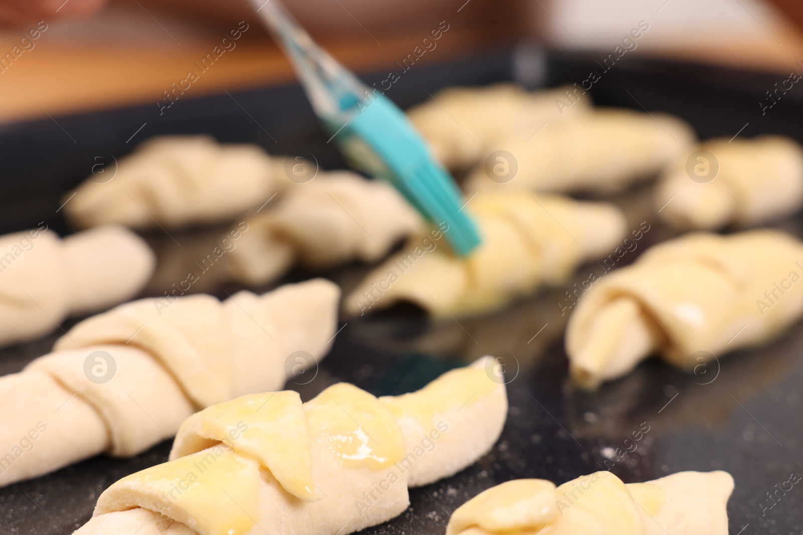 Photo of Woman brushing egg wash onto raw croissants at table indoors, closeup